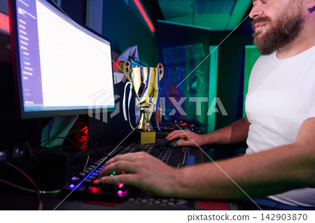 Gamer With Trophy At Computer Celebrating Esports Victory In Neon Gaming Room Gamer With Trophy At Computer Celebrating Esports Victory In Neon Gaming Room 142903870
