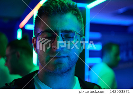 Young Man With Glasses Eyes Closed Bathed in Blue Green Neon Light Nightclub Portrait Young Man With Glasses Eyes Closed Bathed in Blue Green Neon Light Nightclub Portrait 142903871