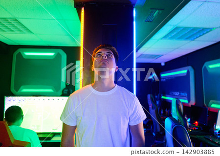 Young Gamer Standing Under Neon Lights in Modern Esports Gaming Room With Computers and Chairs Young Gamer Standing Under Neon Lights in Modern Esports Gaming Room With Computers and Chairs 142903885