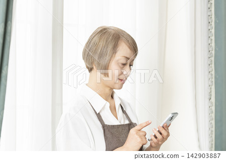 Senior woman skillfully using her smartphone in the living room Senior woman skillfully using her smartphone in the living room 142903887