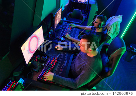 Competitive PC Gamers Playing Esports Together in Neon-Lit Gaming Lounge With RGB Keyboards Competitive PC Gamers Playing Esports Together in Neon-Lit Gaming Lounge With RGB Keyboards 142903976
