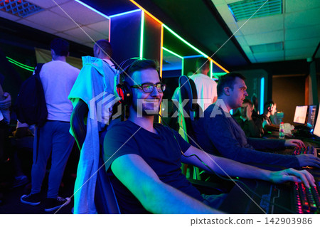 Smiling Young Gamer Playing PC Games at Neon-Lit LAN Party With Friends and Team Smiling Young Gamer Playing PC Games at Neon-Lit LAN Party With Friends and Team 142903986