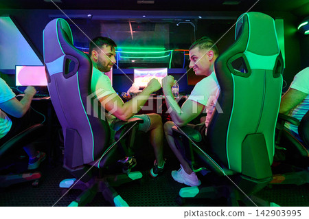Two Friends Gaming and Fist Bumping in Neon Esports Room With PC Gaming Chairs Two Friends Gaming and Fist Bumping in Neon Esports Room With PC Gaming Chairs 142903995