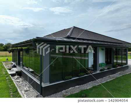 Modern single story house with glass porch and large lawn at sunset in rural setting 142904054