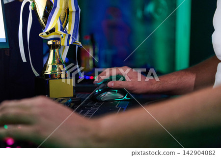 Gamer Hands Using Mouse Beside Trophy After Victory in Competitive Esports Tournament Setup Gamer Hands Using Mouse Beside Trophy After Victory in Competitive Esports Tournament Setup 142904082