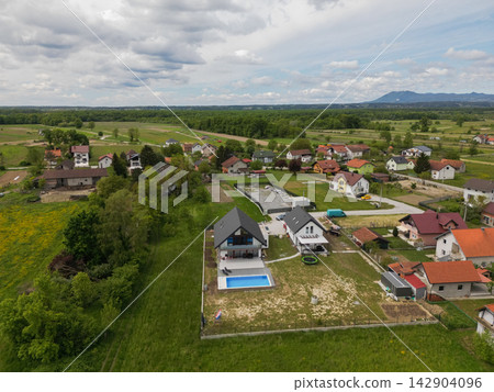 Aerial view of a suburban village with modern houses, backyard pool and green countryside landscape Aerial view of a suburban village with modern houses, backyard pool and green countryside landscape 142904096