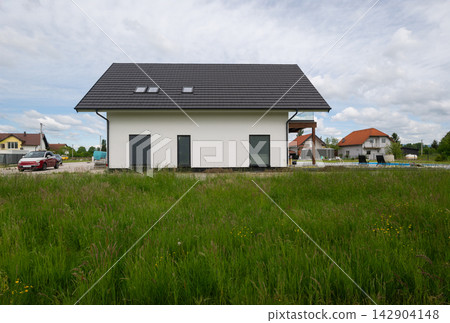 Modern white suburban house with dark roof and meadow in front, contemporary residential exterior Modern white suburban house with dark roof and meadow in front, contemporary residential exterior 142904148