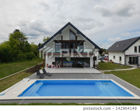 Modern A-frame house with glass balcony and swimming pool in a suburban backyard Modern A-frame house with glass balcony and swimming pool in a suburban backyard 142904149