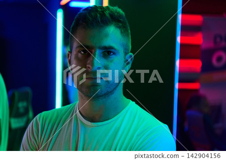 Neon Portrait Of Young Man In Gaming Lounge With Moody Blue And Green Lighting 142904156