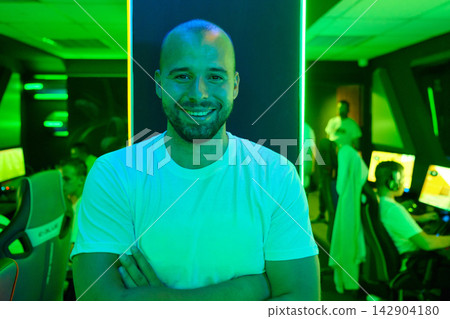 Confident Gamer Standing In Neon Esports Gaming Lounge With Team Playing In Background Confident Gamer Standing In Neon Esports Gaming Lounge With Team Playing In Background 142904180