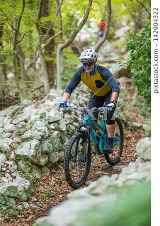 Experienced male cyclist rides a teal mountain bike on a rocky forest trail Experienced male cyclist rides a teal mountain bike on a rocky forest trail 142904322