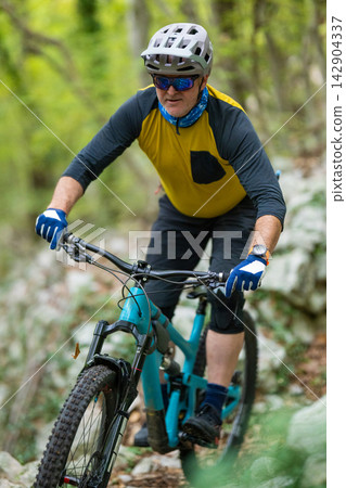 Middle-aged man mountain biking on a forest trail wearing helmet sunglasses and yellow jersey Middle-aged man mountain biking on a forest trail wearing helmet sunglasses and yellow jersey 142904337