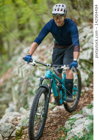 Man mountain biking on rocky forest trail wearing helmet and protective gear Man mountain biking on rocky forest trail wearing helmet and protective gear 142904494