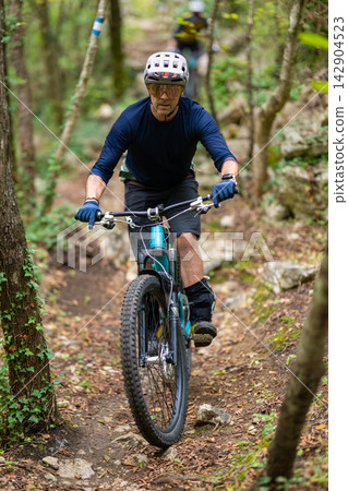 Man mountain biking on a narrow forest trail wearing helmet and protective gear during a summer ride Man mountain biking on a narrow forest trail wearing helmet and protective gear during a summer ride 142904523