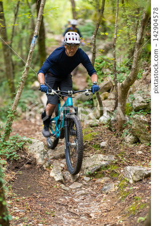 Man mountain biking on rocky forest trail wearing helmet and protective gear Man mountain biking on rocky forest trail wearing helmet and protective gear 142904578