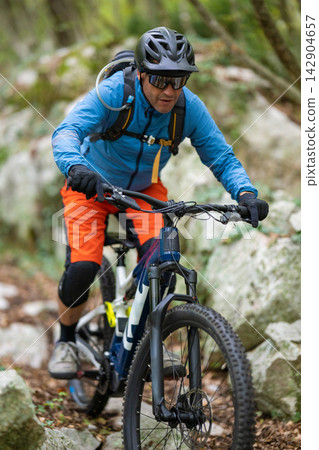 Mountain biking cyclist riding a trail through rocky forest terrain with helmet and backpack Mountain biking cyclist riding a trail through rocky forest terrain with helmet and backpack 142904657