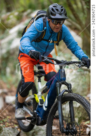 Mountain biker riding a trail through forest wearing helmet, sunglasses and backpack Mountain biker riding a trail through forest wearing helmet, sunglasses and backpack 142904715
