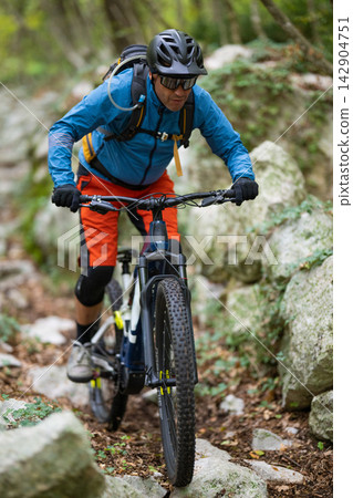 Man mountain biking on a rocky forest trail wearing helmet, sunglasses and hydration backpack Man mountain biking on a rocky forest trail wearing helmet, sunglasses and hydration backpack 142904751