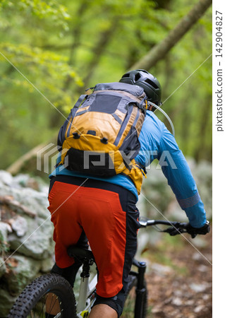 Mountain biker with backpack riding singletrack trail through green forest during outdoor adventure Mountain biker with backpack riding singletrack trail through green forest during outdoor adventure 142904827