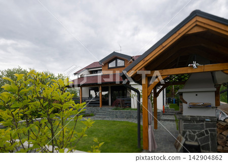 Modern family house with wooden gazebo and patio in landscaped backyard under cloudy sky Modern family house with wooden gazebo and patio in landscaped backyard under cloudy sky 142904862