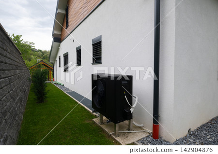 Outdoor heat pump unit next to modern house exterior showing HVAC system and energy-efficient air conditioning Outdoor heat pump unit next to modern house exterior showing HVAC system and energy-efficient air conditioning 142904876