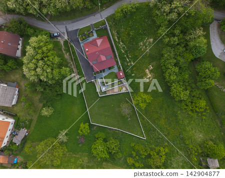 Aerial view of suburban house with red roof and large triangular fenced yard Aerial view of suburban house with red roof and large triangular fenced yard 142904877