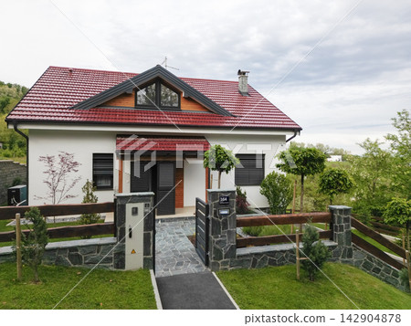 Modern suburban house with red roof, gated entrance and landscaped front yard under cloudy sky Modern suburban house with red roof, gated entrance and landscaped front yard under cloudy sky 142904878