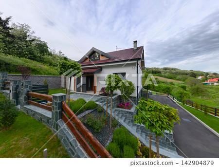 Modern country house exterior with landscaped garden, stone fence and driveway in green hills Modern country house exterior with landscaped garden, stone fence and driveway in green hills 142904879