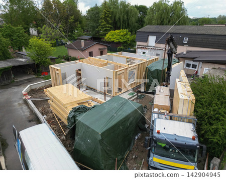 Construction site showing timber frame house assembly with crane, truck and stacked panels in residential area Construction site showing timber frame house assembly with crane, truck and stacked panels in residential area 142904945