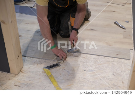Worker installing laminate flooring by hand with hammer and measuring tape during home renovation project Worker installing laminate flooring by hand with hammer and measuring tape during home renovation project 142904949