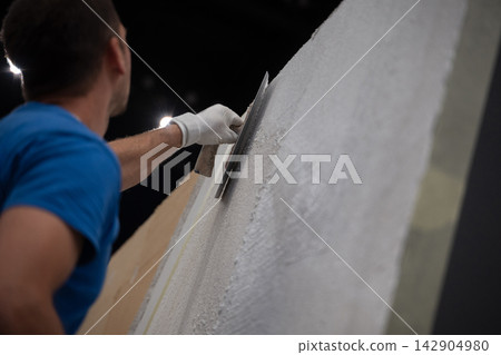 Construction worker plastering an interior wall with a trowel during renovation project Construction worker plastering an interior wall with a trowel during renovation project 142904980