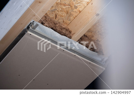 Attic insulation and drywall installation under wooden roof joists during home renovation project Attic insulation and drywall installation under wooden roof joists during home renovation project 142904997