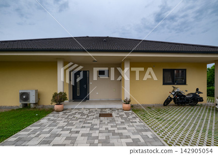 Modern modular home with minimalist facade, low-energy design and motorcycle parked on driveway Modern modular home with minimalist facade, low-energy design and motorcycle parked on driveway 142905054