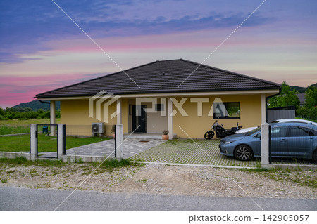 Modern modular home with minimalist facade, low-energy design and driveway parking at sunset Modern modular home with minimalist facade, low-energy design and driveway parking at sunset 142905057