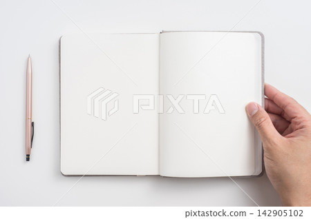 Top view of open blank notebook mockup with hand holding page and pen on white background Top view of open blank notebook mockup with hand holding page and pen on white background 142905102