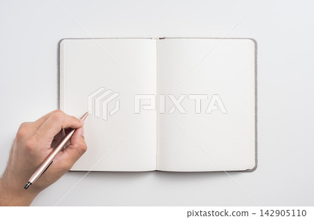 Top view of open blank notebook mockup with hand holding page and pen on white background 142905110
