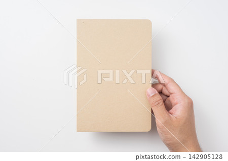 Top view of hand holding closed kraft paper notebook mockup on white background with copy space Top view of hand holding closed kraft paper notebook mockup on white background with copy space 142905128