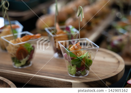Shrimp appetizer served in clear cups on wooden board for catering buffet and party reception Shrimp appetizer served in clear cups on wooden board for catering buffet and party reception 142905162