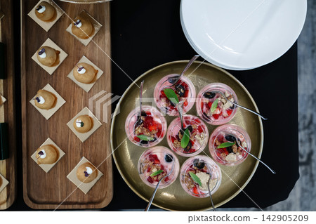 Overhead view of assorted bite-size desserts and berry parfaits on a catering buffet tray Overhead view of assorted bite-size desserts and berry parfaits on a catering buffet tray 142905209