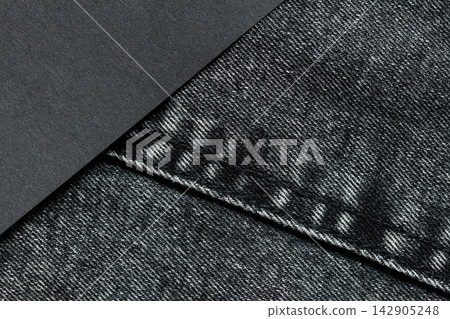 Dark gray paper overlapping a charcoal denim pocket with stitched edges and a diagonal background divide Dark gray paper overlapping a charcoal denim pocket with stitched edges and a diagonal background divide 142905248