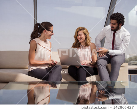 Business team collaborating on laptop during a casual office meeting in a bright modern workspace 142905427
