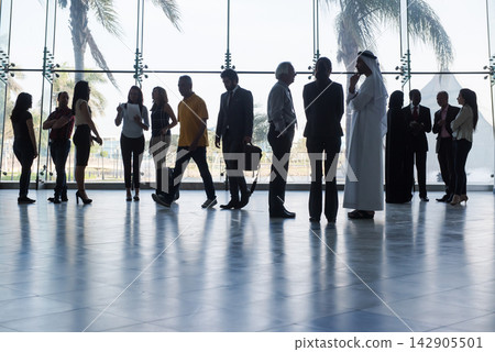 Business people networking and waiting in a spacious glass lobby with palm trees outside Business people networking and waiting in a spacious glass lobby with palm trees outside 142905501