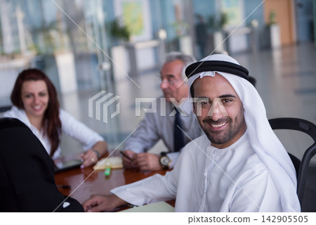 Smiling Emirati businessman at a diverse corporate meeting with colleagues in modern office Smiling Emirati businessman at a diverse corporate meeting with colleagues in modern office 142905505