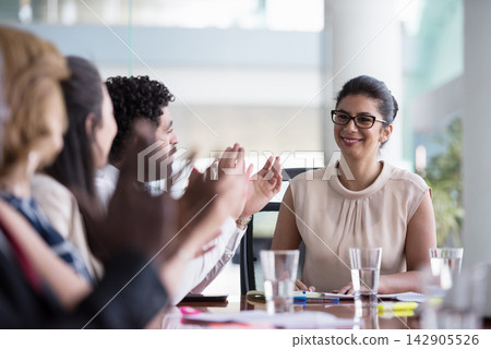 Business team applauding a smiling female leader during a successful office meeting and presentation Business team applauding a smiling female leader during a successful office meeting and presentation 142905526