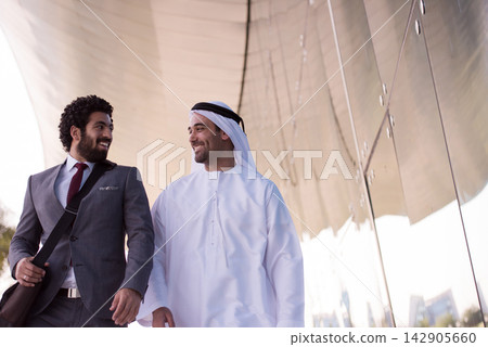 Two businessmen walking and smiling outside a modern glass building, colleagues and friends Two businessmen walking and smiling outside a modern glass building, colleagues and friends 142905660