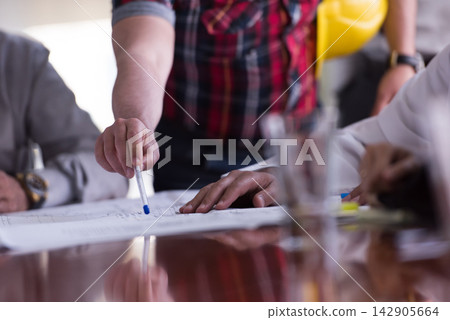 Business team reviewing architectural plans around conference table during construction project meeting 142905664