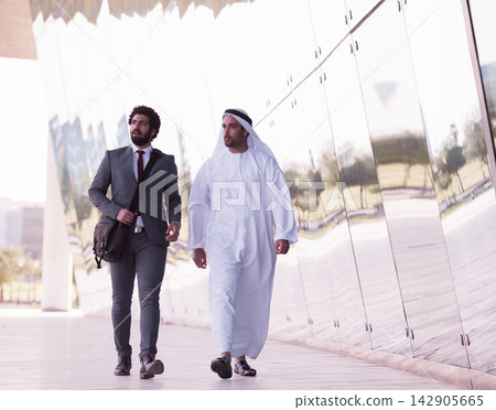 Businessmen walking and talking outside a modern office building, one in suit and one in kandura Businessmen walking and talking outside a modern office building, one in suit and one in kandura 142905665