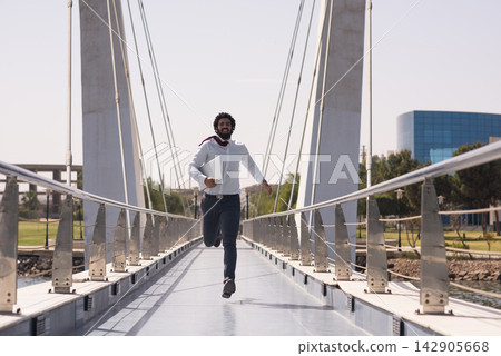 Businessman running across pedestrian bridge with laptop, hurrying to work on a sunny day Businessman running across pedestrian bridge with laptop, hurrying to work on a sunny day 142905668