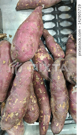 Fresh organic raw purple sweet potatoes in a plastic crate at a market Fresh organic raw purple sweet potatoes in a plastic crate at a market 142905719
