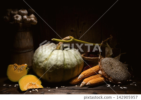 Pumpkins with corn cobs and sunflower on wooden table in moody light Pumpkins with corn cobs and sunflower on wooden table in moody light 142905957